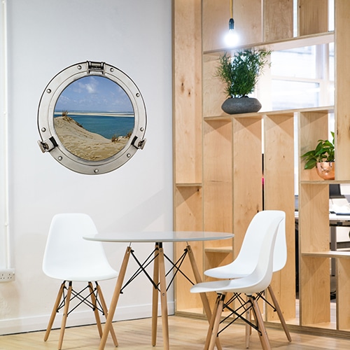 Adhésif mural fenêtre ronde faux hublot de bateau en trompe-l'oeil avec vue sur les dunes du pilat et une eau turquoise dans une salle à manger marine avec un joli claustra de bois.