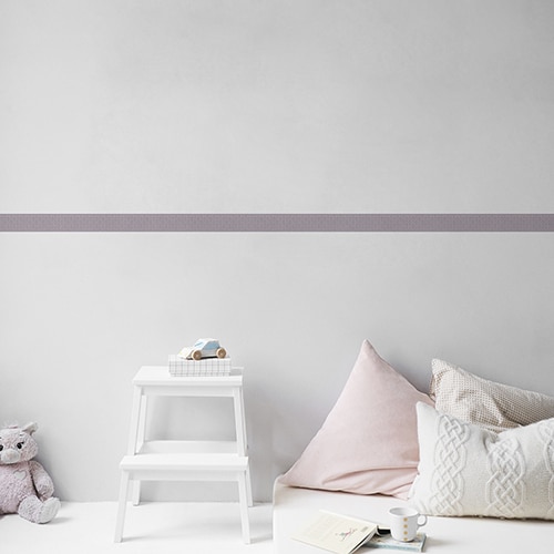 Sticker frise feuille violet et rose dans chambre d'enfant avec coussins et peluche