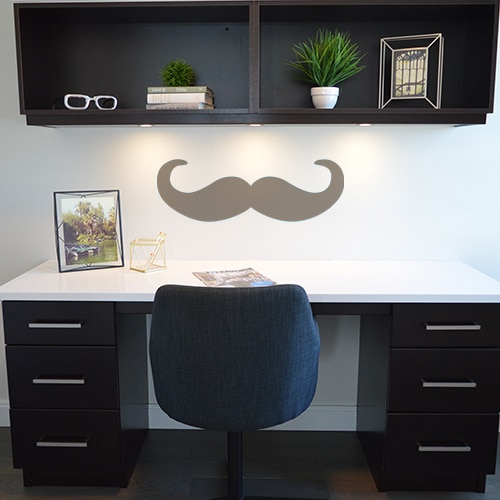Moustache en croc taupe stickée sur un mur de bureau blanc
