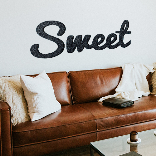 Sticker adhésif citation Sweet au dessus d'un canapé en cuir marron