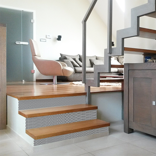 Escalier en bois clair personnaliser avec des stickers pour contremarches d'escalier au motif chevrons 3D en gris et blanc.
