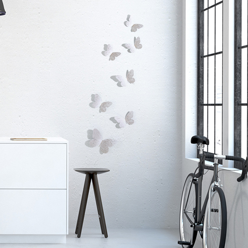 Stickers papillons manuscrits en 3D sur un mur de salon avec un vélo et une fenêtre