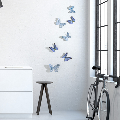 Stickers papillons mix bleu et liberty en 3D sur mur de salon avec un vélo et une fenêtre