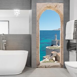 Dans une salle de bain moderne grise et blanche on s'évade à l'aide de cet adhésif pour porte qui nous emmène au bord de la Méditerranée dans une vieux village entouré d'une forteresse