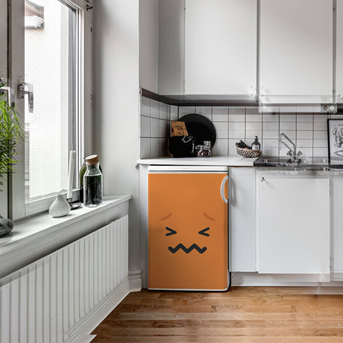 Petit frigo classique orné d'un sticker adhésif pour électroménager Smiley Tracas Orange dans une cuisine blanche